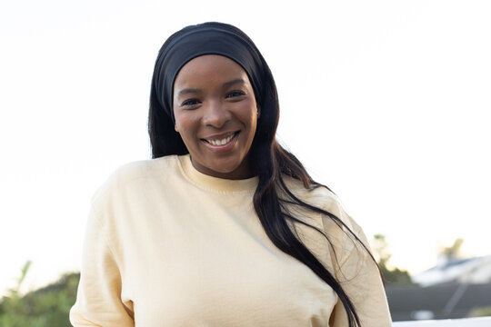 African American woman smiling in backyard wearing cream top and black headband with stud earrings