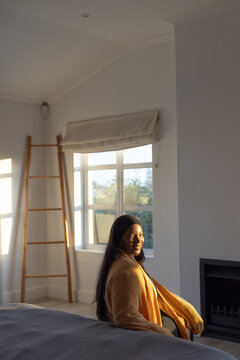 African American woman mustard knit sitting on chair by bed ladder sunlight hitting face