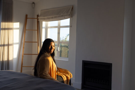 African American woman sitting in bedroom chair near bed, wearing mustard cardigan, wooden ladder