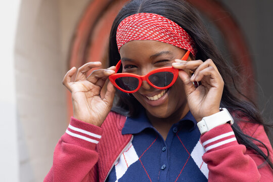 African American woman adjusting red cat-eye sunglasses, winking, smiling with headband at doorway