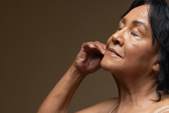 Senior African American woman tilting back, eyes closed in studio lighting, strap top, copy space