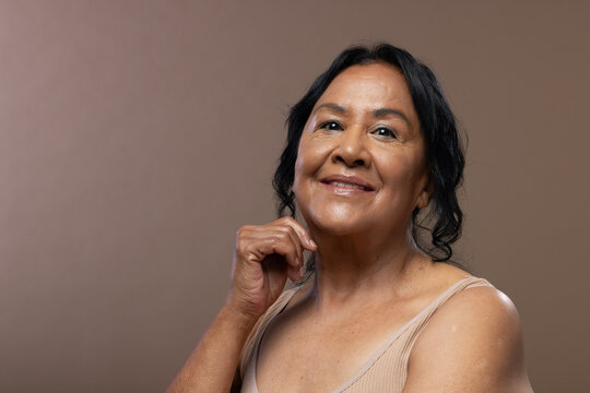 Senior African American woman smiling posing in studio in sleeveless beige top with warm backdrop