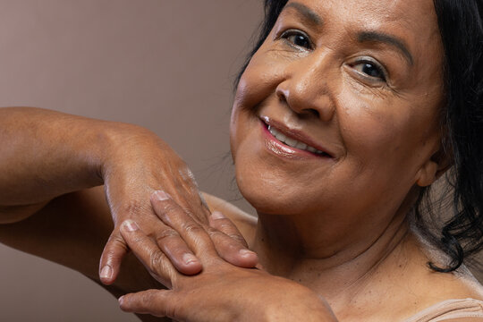 Senior African American woman wearing beige top smiling and resting hands by shoulder in studio