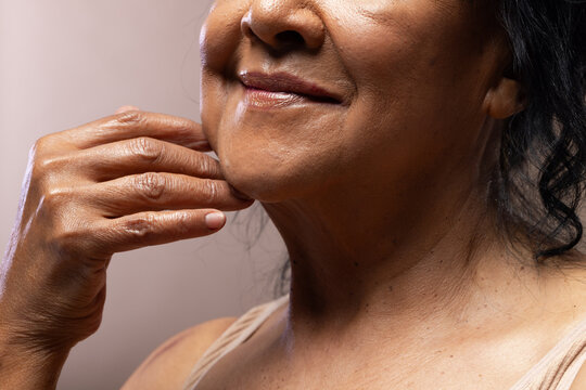 Senior African American woman resting right hand on chin, wearing thin-strap top in studio