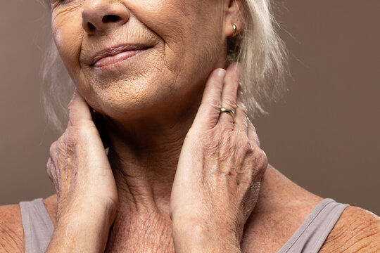 Senior female touching neck, wearing sleeveless top, gold hoop earring and wedding band in studio
