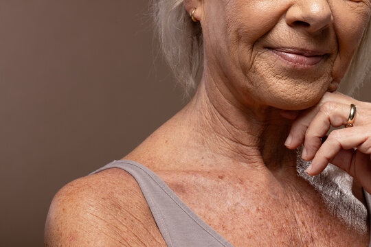 Senior woman posing in studio, touching chin and showing gold wedding band, hoop earring, taupe top