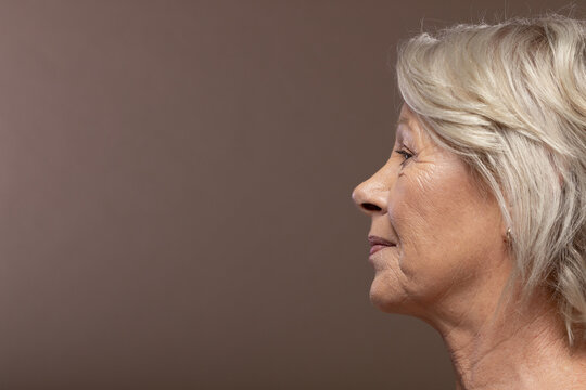Senior woman posing in studio with brown backdrop, showing small stud earring, copy space