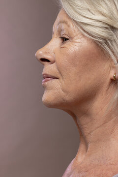 Senior female posing in studio showing right profile with bare neck, hoop earring and warm backdrop