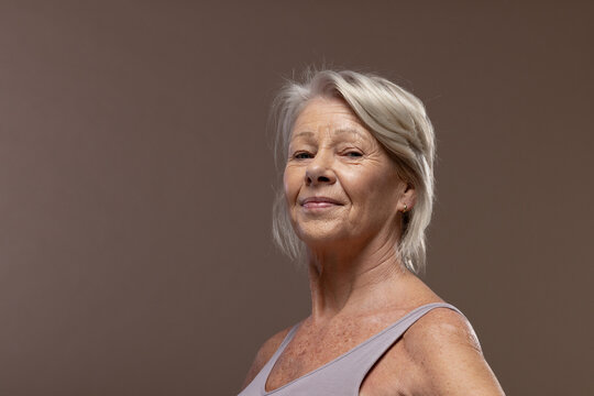 Senior female posing in studio backdrop, wearing mauve tank and stud earring, getting studio light