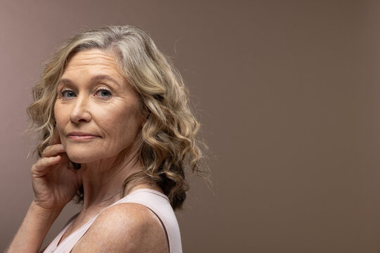 Mature female turning shoulder in studio wearing pale sleeveless top, thin chain necklace
