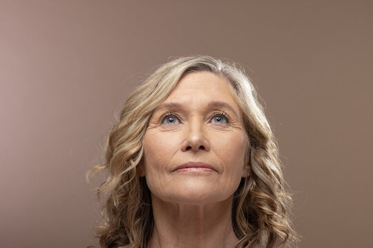 Mature female posing in studio, facing forward and looking upward with soft beige backdrop