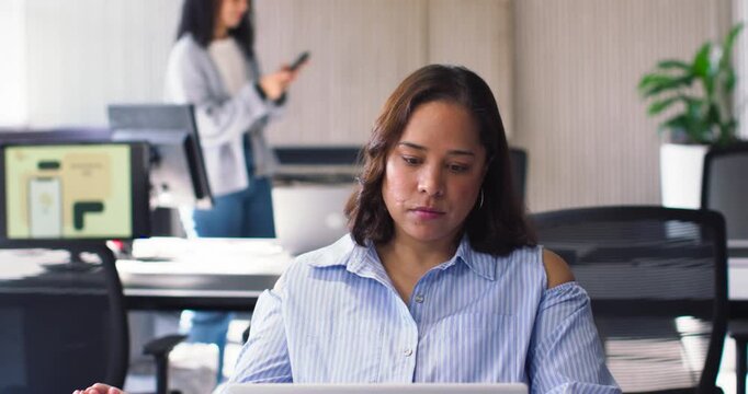 African American women in open office, coworker checking phone causing front woman typing on laptop