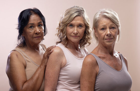 Senior and mature women holding gaze in studio with pale pink seamless backdrop, wearing tank tops