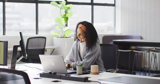African American woman pausing from typing at laptop in office, adjusting pen cup, scrolling phone