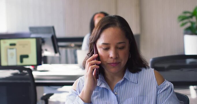 Female team foreground-woman in striped top answering work call on phone glancing notes smiling