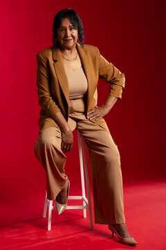 Senior African American woman sitting on white stool in studio wearing tan suit and heels