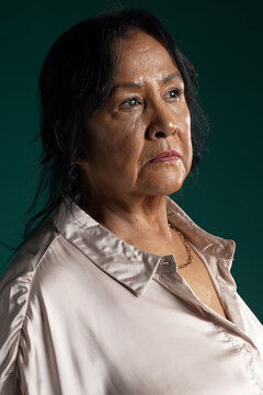 Senior female posing and gazing right in portrait studio wearing pale satin blouse and gold chain