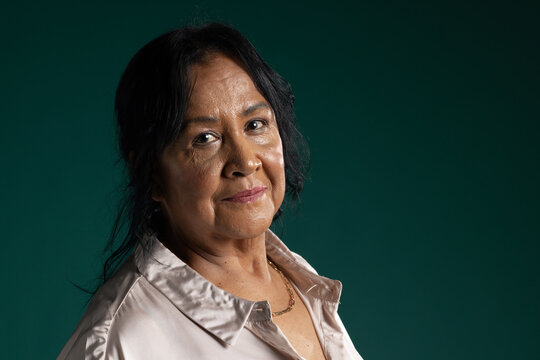 Senior African American woman posing in studio with teal backdrop, wearing satin blouse, gold chain