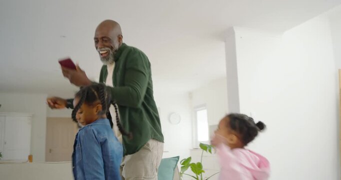 African family man holding smartphone, playing music and leading two child girls dancing at home