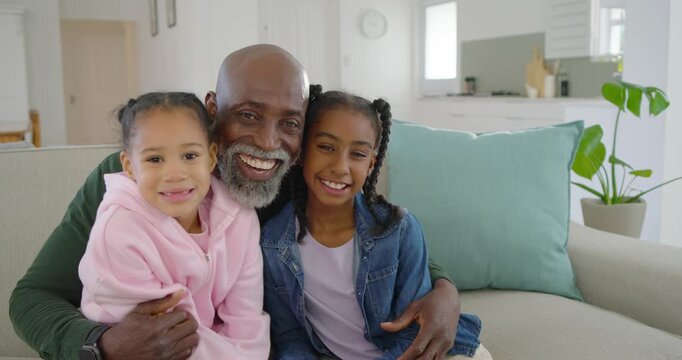 African American man with two girls sharing smartphone clip, laughing and hugging on couch at home