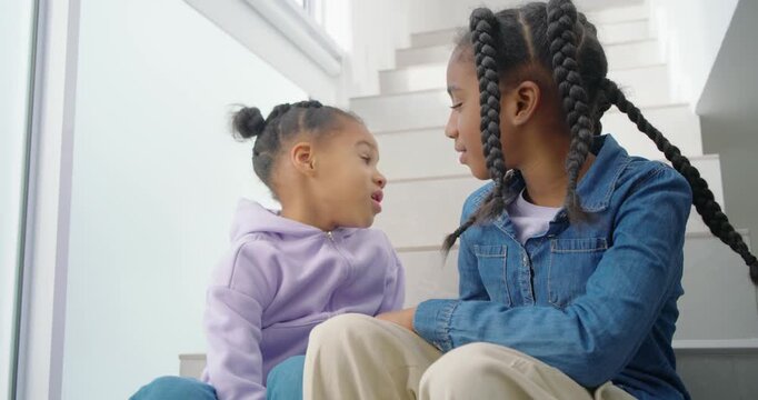 African American girls sitting on stairs by window younger leaning, confiding while older listening