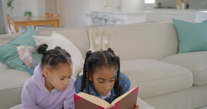 African American girls reading on couch, right reader opening red book to share story, denim jacket
