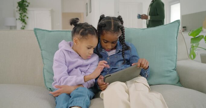 African family father holding mug while left child tapping tablet, siblings sharing tablet at home