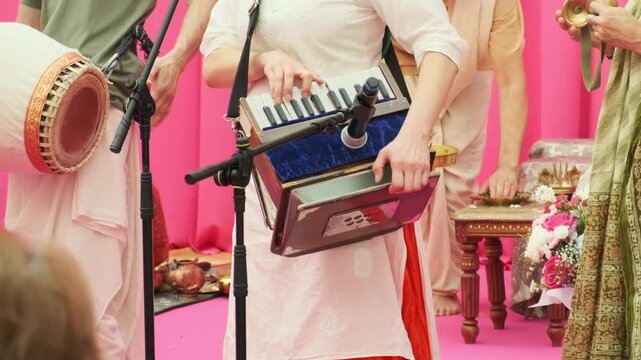 musician playing harmonium during live kirtan performance. devotees dancing hare krishna during spiritual kirtan. joyful kirtan creates peaceful atmosphere for spiritual group gathering