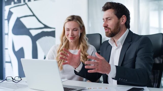 Two Caucasian business partners happy professional man presenting laptop data to woman working insurance service investing work businessman talk present computer task to businesswoman at office table