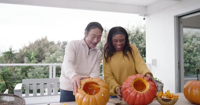 Diverse couple with senior member scooping seeds, lids removed, carving pumpkins on porch for decor
