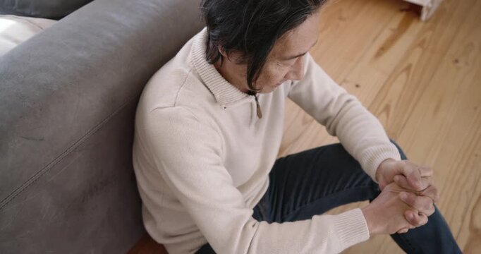 After clasping hands, Senior Japanese man adjusting grip, rubbing, stretching beside sofa at home
