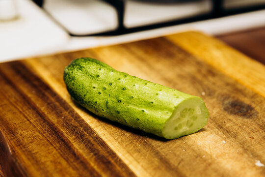 Fresh sliced cucumber on wooden cutting board close up, green vegetable prepared for cooking in kitchen, healthy food ingredient on rustic wood surface.