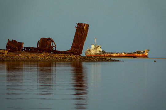 The rusted skeleton of a shipwreck rises from the water beside another stranded vessel, Northern Red Sea, Massawa, Eritrea