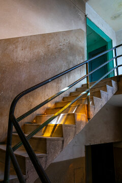 Sunlight streaks across a concrete staircase inside a weathered building with a teal painted door, Central Region, Asmara, Eritrea