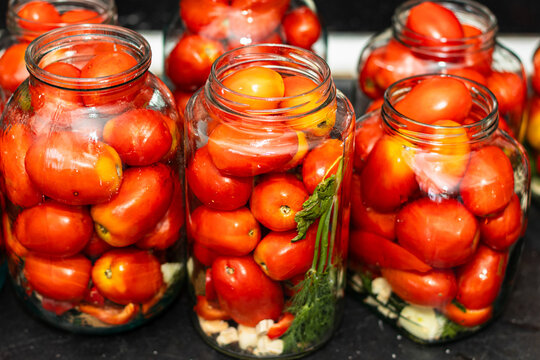 Jars filled with ripe red tomatoes and fresh herbs arranged on a kitchen countertop, showcasing home canning and preservation techniques for seasonal produce