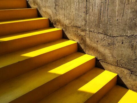 Minimalist yellow staircase with geometric sun shadows and textured concrete wall