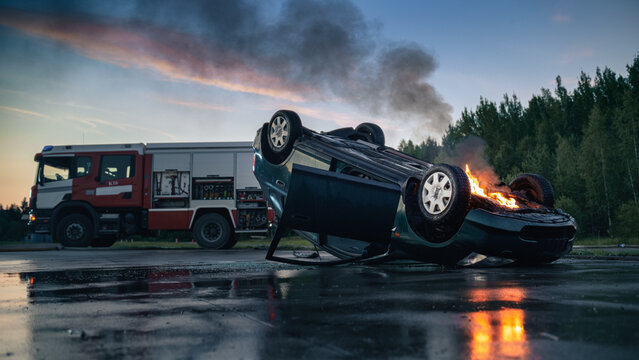 Upside Down Car Burning With Fire and Black Smoke on Road After Traffic Accident, Fire Engine Parked at Car Crash Site Waiting for Firefighters and Rescue Workers to Start Emergency Operation