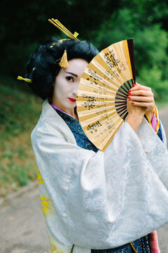Close up portrait of a woman with geisha makeup holding a traditional Japanese fan