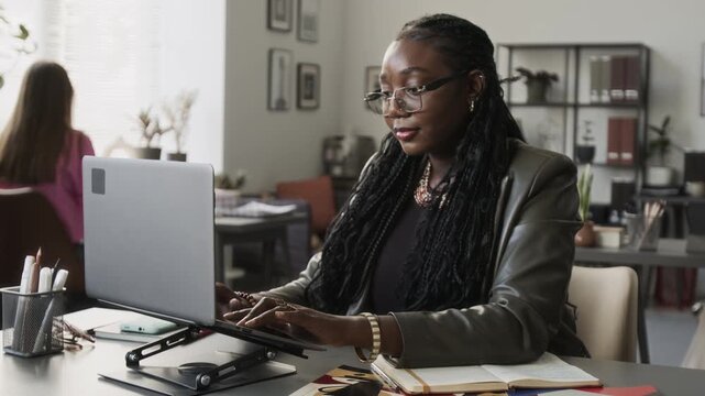 African American young adult woman typing on laptop at workplace desk. Perfect for corporate communication, tech tutorials, and digital business promotions