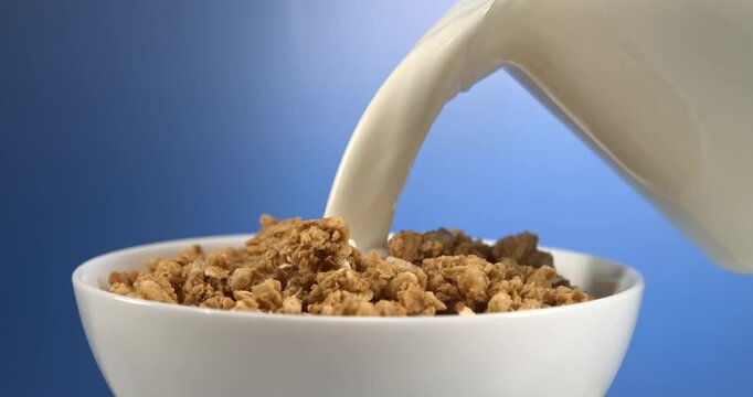 Milk pouring onto granola in bowl for breakfast in slow motion close up