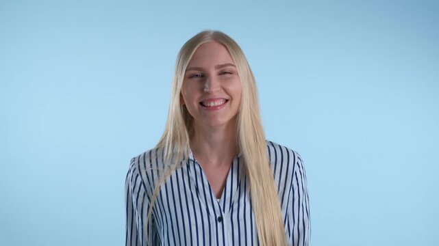 A young blonde woman wearing a striped shirt raises her fists and cheers with excitement against a solid blue background in a studio setting.