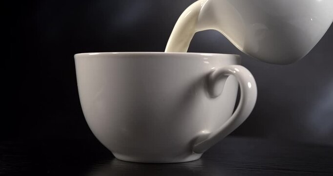 Cream pouring into a white cup in slow motion on black background