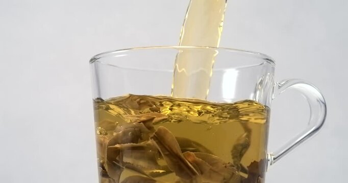 Hot green tea pouring into glass cup with tea leaves and steam in slow motion
