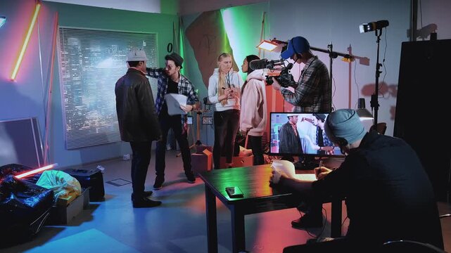 A group of film crew members and talent engage in discussion and technical setup inside a professional indoor studio environment.