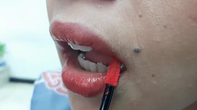 Close-up of a woman applying orange lip cream on her lips using a wand applicator