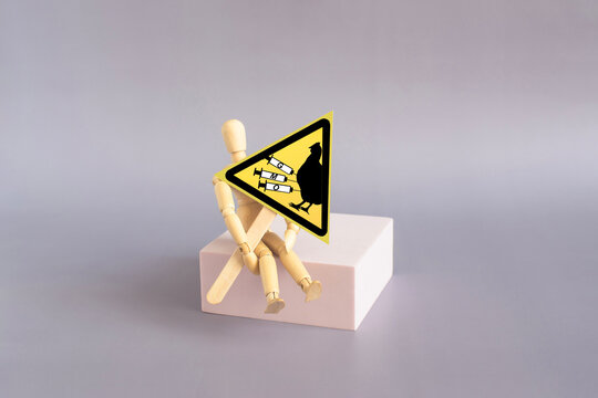 The doll is holding a warning sign that reads &ldquo;Dangerous genetically modified products in chicken meat&rdquo; in the form of a yellow triangle, shot in close‑up against a light background.