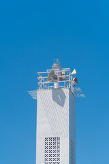 White lighthouse stands tall against clear blue sky. Metal framework frames its beacon at top. Calm, uncluttered scene exudes serenity. Ideal for travel, coastal, or maritime themes © Rizky Rahmat Hidayat