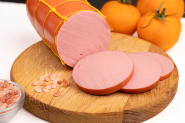 Sliced boiled sausage background closeup with fresh ham slices on wooden cutting board, organic pork meat product with peppercorn mix, pink salt and yellow tomatoes, horizontal studio e-commerce copy  © Inna Nikitina