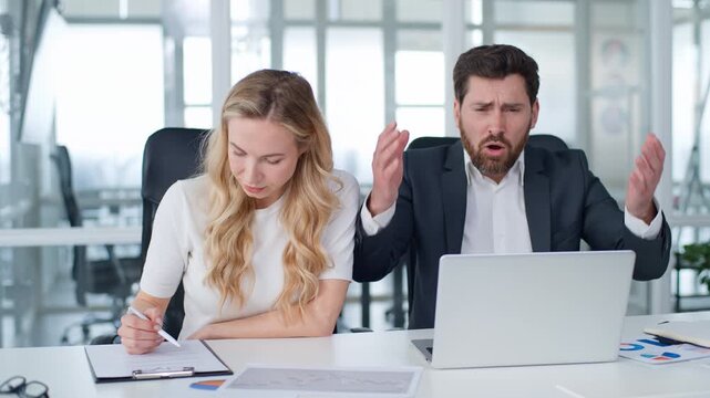 Caucasian business team two coworkers upset with laptop woman writing in papers looking at screen with frustrated man businesswoman with businessman worried with working computer failure in office