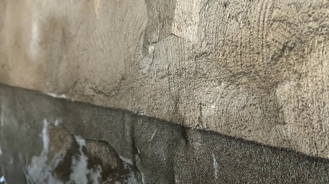 Close up of rough old plaster wall texture with cracks. Candid camera pan right shot of weathered building surface with gritty structural details in natural light.